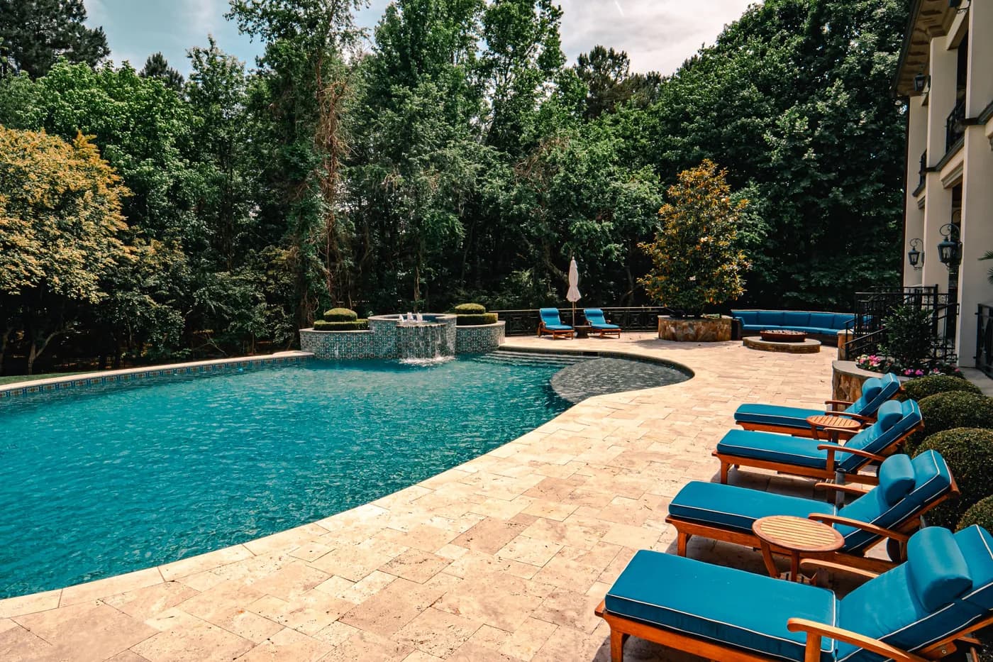 Backyard swimming pool with stone decking and blue lounge chairs